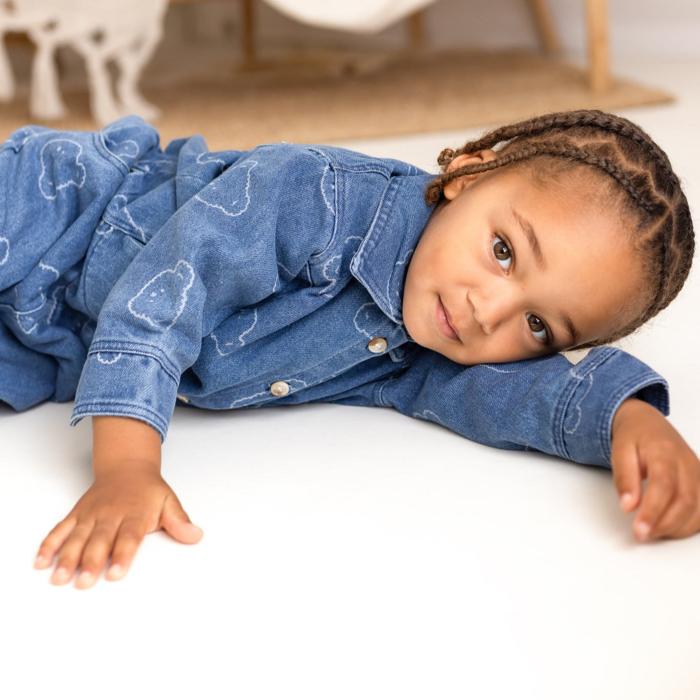 Child wearing a blue denim outfit lying on a white surface with a blurred background