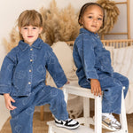 Two children wearing matching denim outfits sitting on a small white stool.
