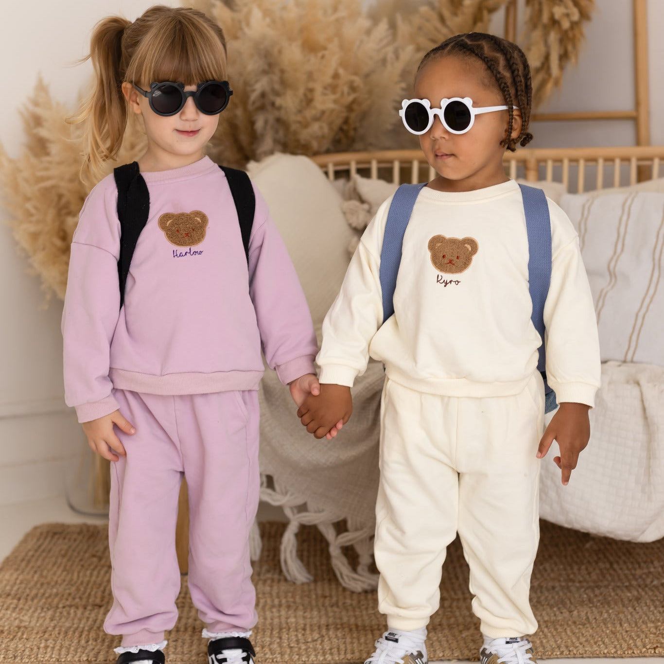 Two children holding hands, wearing matching outfits with heart designs in a cozy indoor setting.