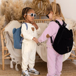 Two children in matching outfits with backpacks shaking hands in a cozy room.