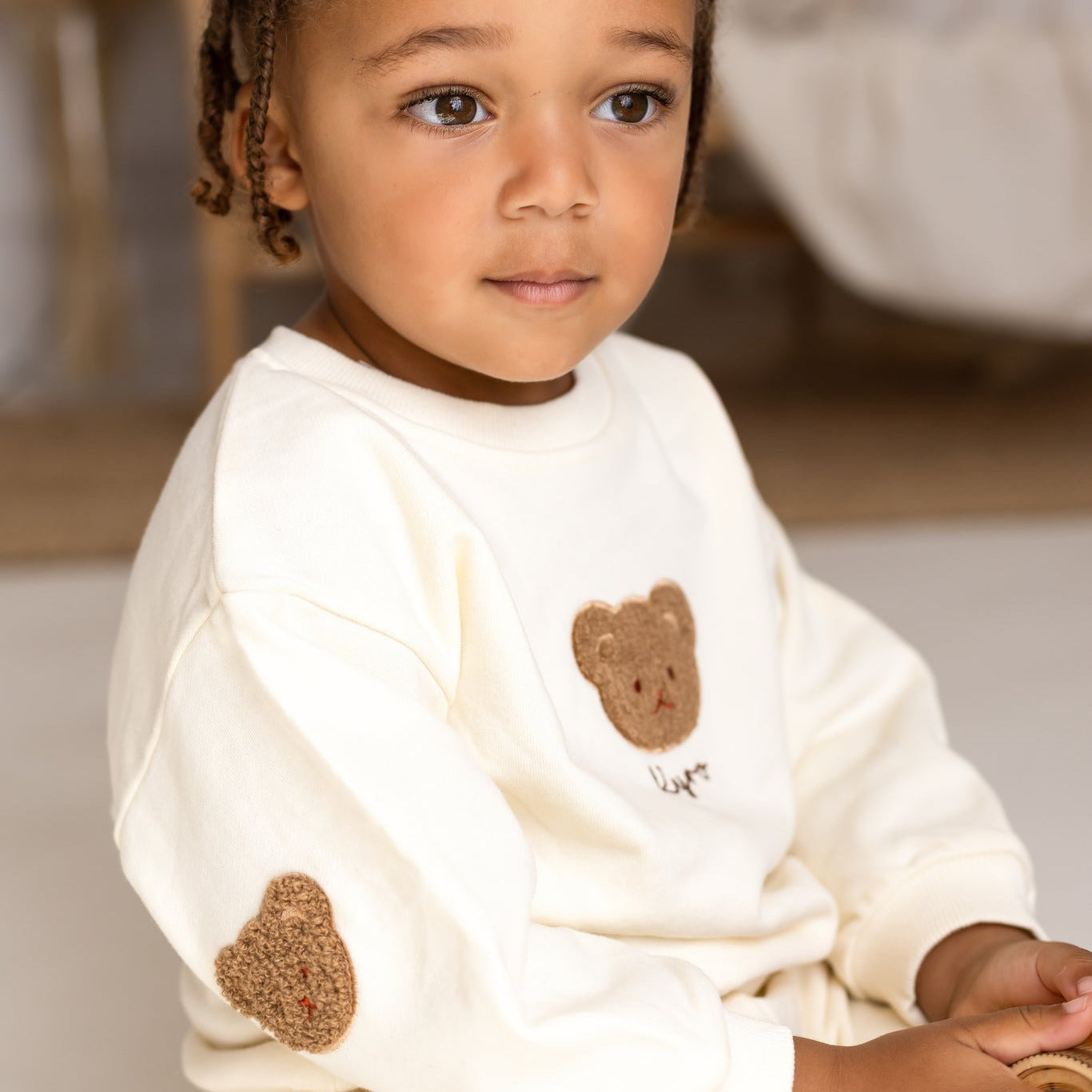 Child wearing a white outfit with bear designs in a blurred indoor setting