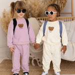 Two children holding hands, wearing matching outfits with heart designs in a cozy indoor setting.