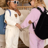 Two children in matching outfits with backpacks shaking hands in a cozy room.  The Bear Backpack Bag Personalised Cozy Crew Club Bags mora-uk.myshopify.com the-bear-backpack-bag   10off, 20off, acc, accessories, accessory, allproducts, baby, back pack, backpack, bag, beige, BFCM-20, BFCM-25, BFCM20, birthday, china, CHRISTMAS20, clothing, daywear, embroidery, kids, LINECARD, lunch box, new in, PADDY10, personalised, school, set, slip on, whatnot, WINTER20, zero